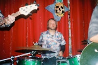 a man playing drums in front of a red curtain